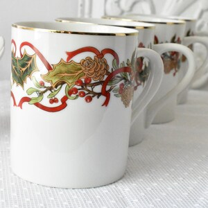 May include: Set of four white ceramic mugs with a gold rim and a festive holiday design featuring red ribbons, green holly leaves, and red berries.