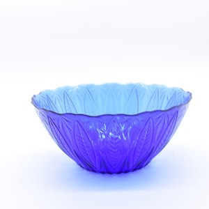 May include: A blue glass bowl with a leaf pattern. The bowl is empty and sitting on a white surface.
