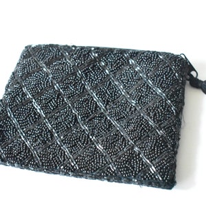 Puede incluir: Un clutch negro de cuentas con un borla. El clutch tiene un patrón de diamantes y está hecho de pequeñas cuentas negras.