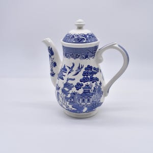 May include: A white and blue ceramic coffee pot with a lid. The pot features a classic blue and white Willow pattern design with a spout and handle. The pot is approximately 25 cm tall.