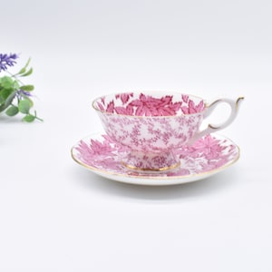 May include: A pink and white teacup and saucer set with a floral pattern. The cup and saucer have a gold trim.