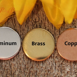May include: Three round metal discs, each with a different finish: aluminum, brass, and copper. The discs are arranged horizontally on a wooden surface.