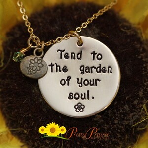 May include: A silver necklace with a round pendant that says "Tend to the garden of your soul." The pendant has a small flower charm attached to it.