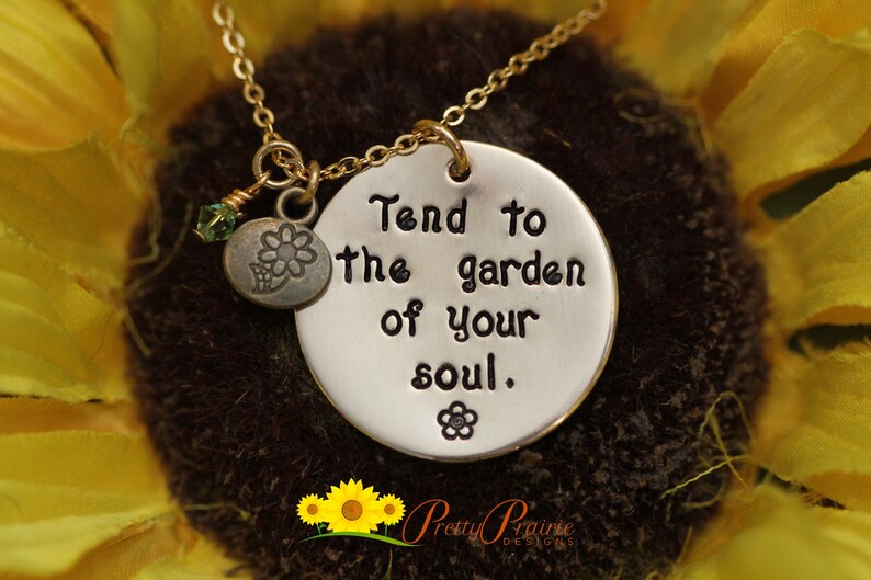 May include: A silver necklace with a round pendant that says "Tend to the garden of your soul." The pendant has a small flower charm attached to it.