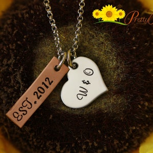 May include: A silver necklace with a heart charm engraved with "W & O" and a brown leather tag engraved with "EST. 2012".