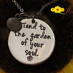 May include: Silver necklace with a round pendant that says "Tend to the garden of your soul." The pendant has a small flower charm attached to it.