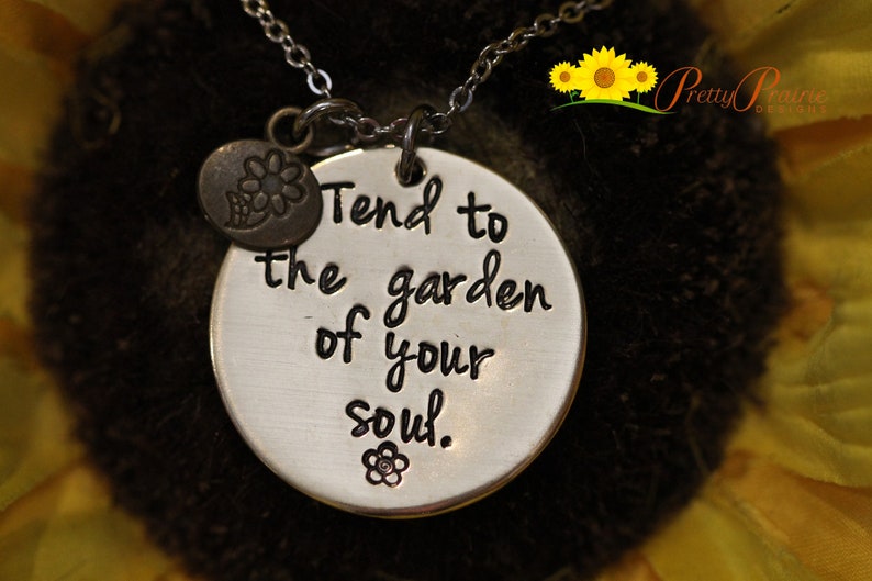 May include: Silver necklace with a round pendant that says "Tend to the garden of your soul." The pendant has a small flower charm attached to it.