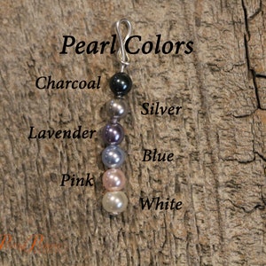 May include: A close-up of a string of pearls in various colors, including charcoal, silver, lavender, blue, pink, and white. The pearls are strung on a silver wire and are labeled with their corresponding colors.