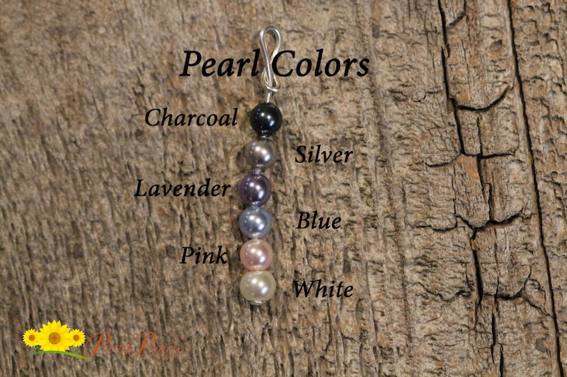 May include: A close-up of a string of pearls in various colors, including charcoal, silver, lavender, blue, pink, and white. The pearls are strung on a silver wire and are labeled with their corresponding colors.