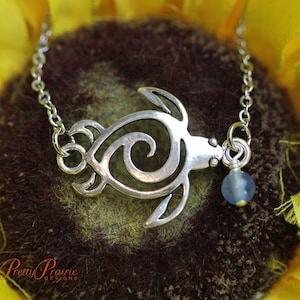 May include: A silver chain necklace with a silver turtle pendant and a blue glass bead. The turtle is a stylized design with a swirl inside.