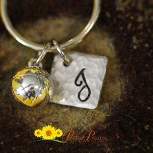 May include: A silver keychain with a basketball charm and a square charm with the letter "J" engraved on it. The charms are attached to a silver ring.