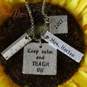 May include: Silver necklace with four charms: a ruler, a square charm that says "Keep calm and TEACH ON", a rectangular charm that says "Mrs. Horton", and a square charm that says "2017".
