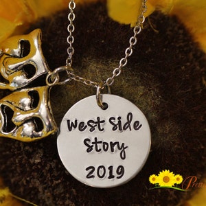 May include: A silver necklace with a round charm that says "West Side Story 2019" and a charm of two silver theater masks.
