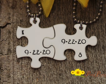 May include: Two silver puzzle pieces on a wooden surface. The pieces are connected and have the date 9-22-20 engraved on them. One piece also has the letter K engraved on it and the other has the number 8 engraved on it.