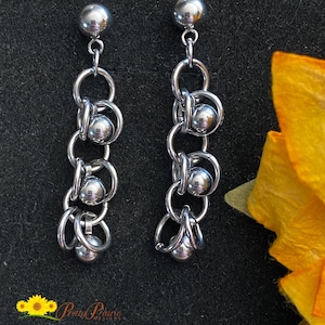 May include: A pair of silver earrings with a chain design and multiple round beads. The earrings are dangling and have a simple, modern style.