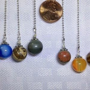 May include: Assortment of eight different gemstone and agate beads on silver chains. The beads are various colors and patterns, including brown, blue, green, red, orange, and gray.