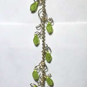 May include: A gold chain with green leaf-shaped beads hangs from a brown beaded sunflower. The sunflower has a dark brown center.