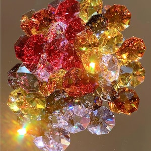 May include: A collection of faceted gemstones in various colors, including red, yellow, orange, and clear. The gems are arranged closely together, reflecting light and creating a sparkling effect. The shapes are irregular, with multiple facets.