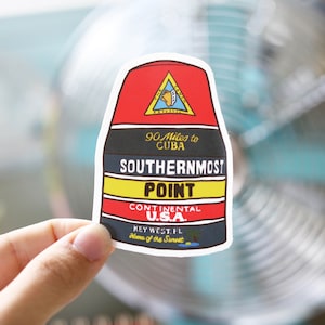 Puede incluir: Una pegatina en forma de boya roja, blanca y negra con el texto "90 Miles to CUBA", "SOUTHERNMOST POINT", "CONTINENTAL U.S.A.", "KEY WEST, FL" y "Home of the Sunset".