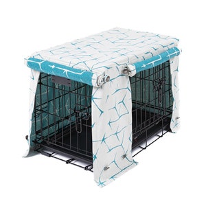 May include: A teal and white patterned fabric dog crate cover with a zippered top and side panels. The cover is designed to fit over a standard wire dog crate.