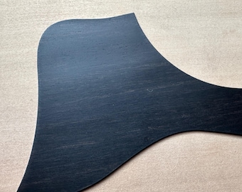 May include: A black guitar pick made of wood with a smooth, slightly textured surface.