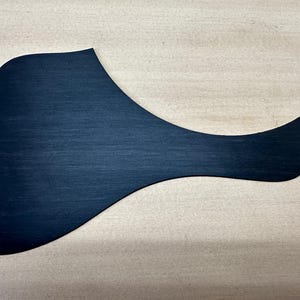 May include: A dark blue guitar pickguard with a unique shape, designed to protect the guitar's body from scratches. The pickguard has a smooth, matte finish and is made of a solid material.