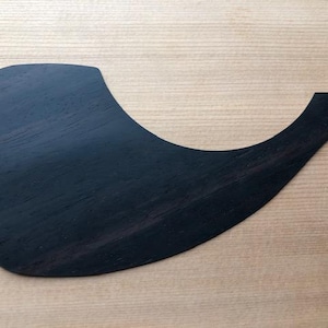 May include: A dark brown wood guitar pickguard with a curved shape.
