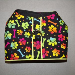 May include: A black dog harness with a bright rainbow paw print and bone pattern. The harness has a lime green trim and a silver metal ring.