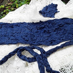 May include: A blue fabric headband with a braided tie. The headband is on a white lace background.