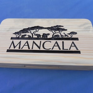 May include: A wooden box with a carved design of trees and animals. The box is labeled "MANCALA".