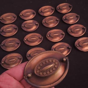 May include: A set of 17 antique brass oval cabinet knobs with a decorative design. The knobs have a slightly aged finish and are perfect for adding a vintage touch to any home decor project.