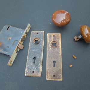 May include: Antique door hardware set with two ornate brass plates, a black metal latch, and two brown ceramic door knobs.