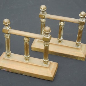May include: A pair of antique brass fireplace andirons with fluted columns and decorative finials. The andirons are in good condition with a warm, aged patina.