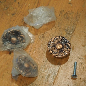 May include: Three ornate copper cabinet knobs with a floral design, packaged in plastic bags, and a single screw.