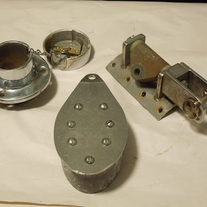 May include: Three silver metal boat hardware pieces. One is a round, flat, circular piece with a smaller, round, hollow cylinder in the center. Another is a long, oval-shaped piece with a hole at the top and eight small, round holes on the surface. The third piece is a rectangular, flat piece with a metal arm extending from the side. The arm has a small, round, hollow cylinder at the end.