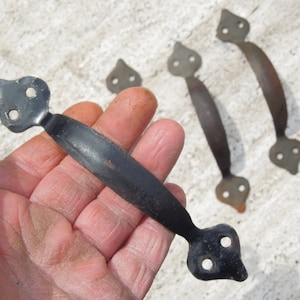 May include: Four black metal door handles with a decorative pointed design. The handles have two holes for mounting.