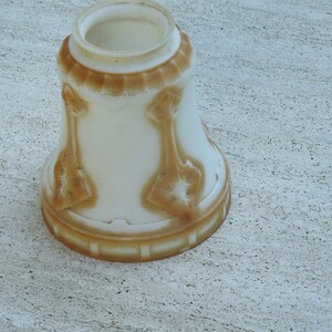 May include: A white glass lampshade with a brown, decorative pattern. The shade has a wide, round opening at the top and a narrow base.