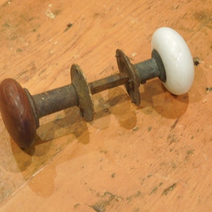 May include: A vintage door knob with a wooden and porcelain design. The knob is made of metal and has a brown wooden handle and a white porcelain knob.