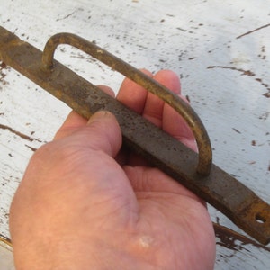 May include: A rusty metal handle with a loop for a door or drawer. The handle is about 10 inches long and has a rough, aged texture.