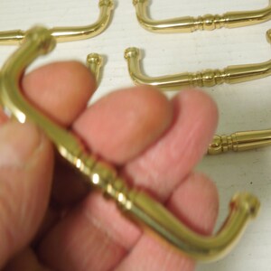 May include: A set of five gold-toned cabinet pulls with a decorative ribbed design. Each pull has a rounded, slightly curved shape.