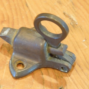 May include: A vintage brass window latch with a ring handle. The latch is designed to secure a window from the inside.
