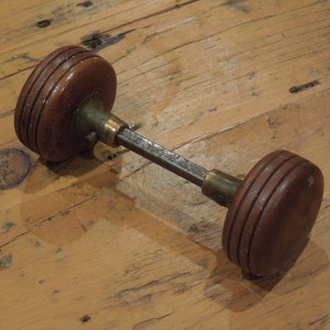 May include: A vintage door knob with a wooden handle and a metal spindle. The knob is brown and has a grooved design. The spindle is silver and has a brass finish.