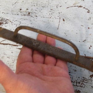 Może przedstawiać: Metalowy uchwyt zardzewiały z pętlą do drzwi lub szuflady. Uchwyt ma około 38 cm długości i ma szorstką, fakturowaną powierzchnię.