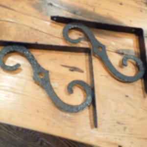 May include: Two black metal shelf brackets with a decorative scroll design. The brackets are made of sturdy metal and have a rustic finish.