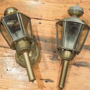 May include: Two antique brass wall-mounted lanterns with clear glass panels and a decorative finial on top.