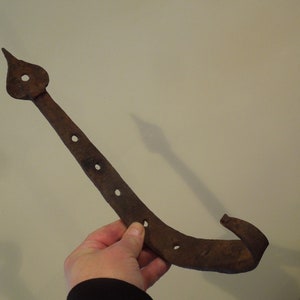 May include: A rusty metal hook with a pointed end and a curved hook at the other end. The hook has five holes along its length.