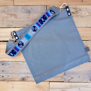 May include: A gray canvas bag with a colorful woven strap. The strap has a geometric pattern in shades of blue, gray, and red.