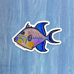 May include: A colorful sticker featuring a cartoon fish with blue, yellow, and purple hues. The fish has a distinctive fin shape and is outlined in black. The text "@dangcutefish" is printed on the sticker.