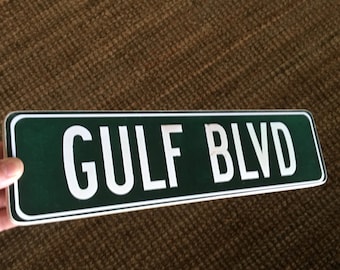 May include: A green and white street sign with the text "GULF BLVD" in white letters.