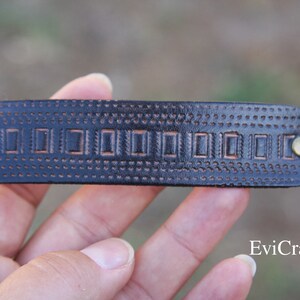 May include: A dark brown leather hair barrette with a rectangular shape. The barrette features a series of embossed rectangular designs and small dot patterns. Two brass-colored rivets secure the barrette.